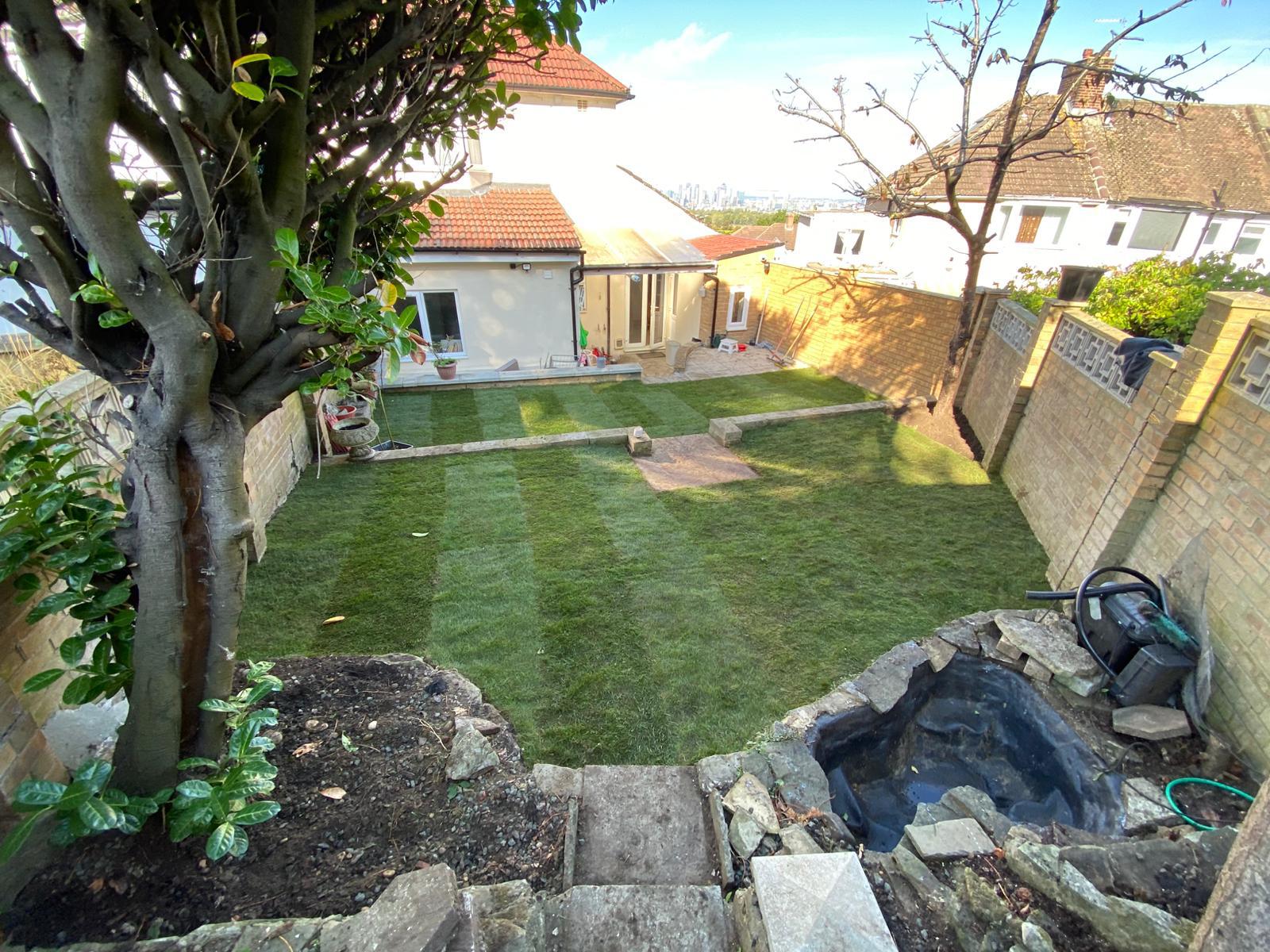 Long walled garden re-turfed with a new lawn viewed from steps beside a small pond.