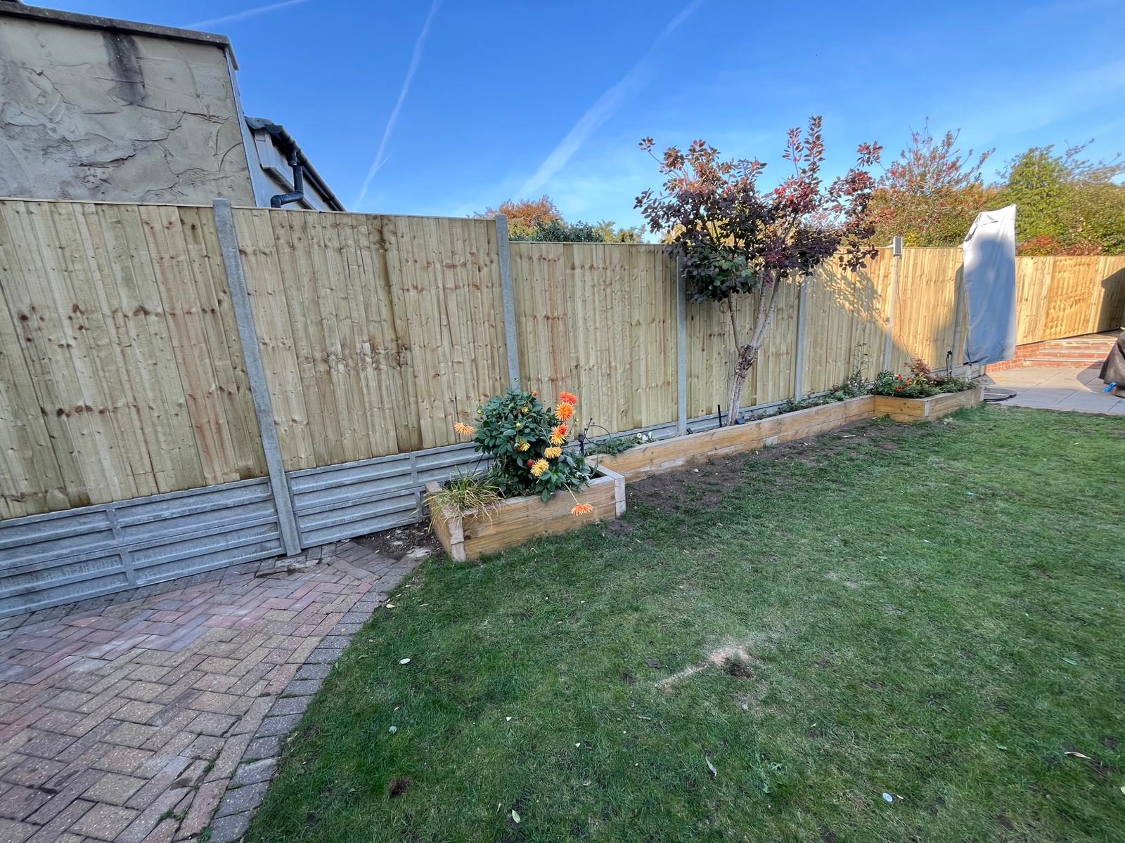 Back garden with new fence, sleeper planter and lawn.