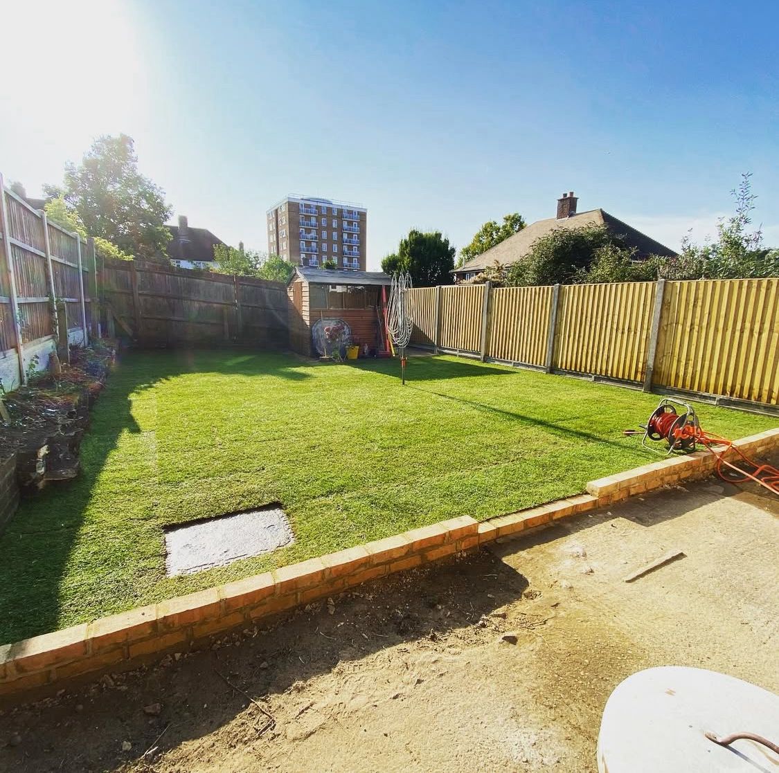 Long, level lawn with sleeper edging and a garden building at the end.